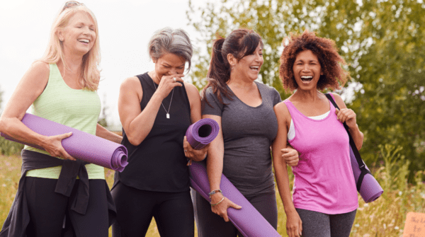 a group of four women walking together after a yoga exercise, holding mats and laughing and smiling