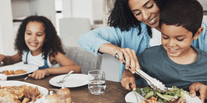 Mom serving a smiling child a healthy meal with another child smiling in the background