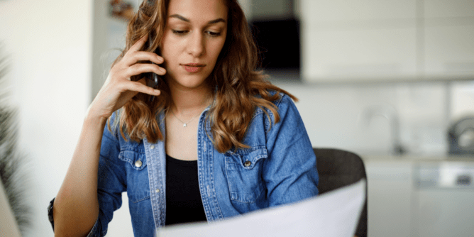 woman looking at a bill and laptop while on the phone