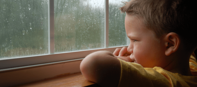 young boy looking out the window while it's raining