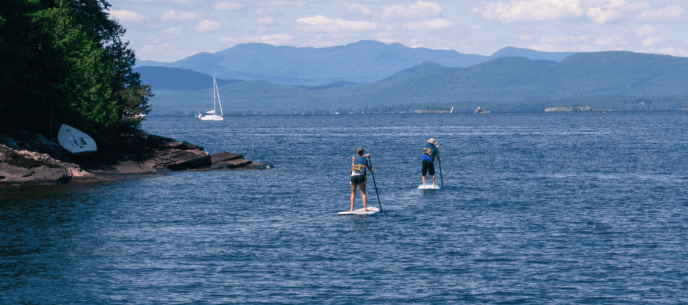 two people stand up paddle boarding with mountains in the background