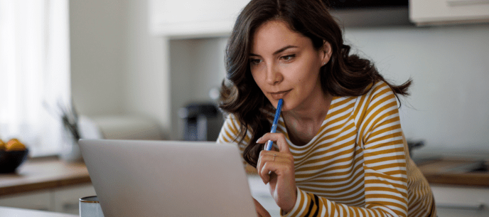 woman holding a pen and looking at her computer looking contemplative
