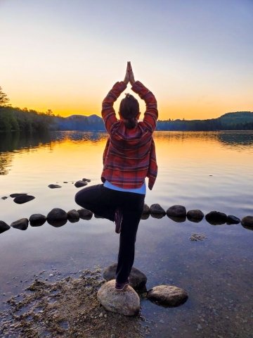 Christine Badalamenti Smith holding a yoga pose on a rock in front of a sunrise on a lake